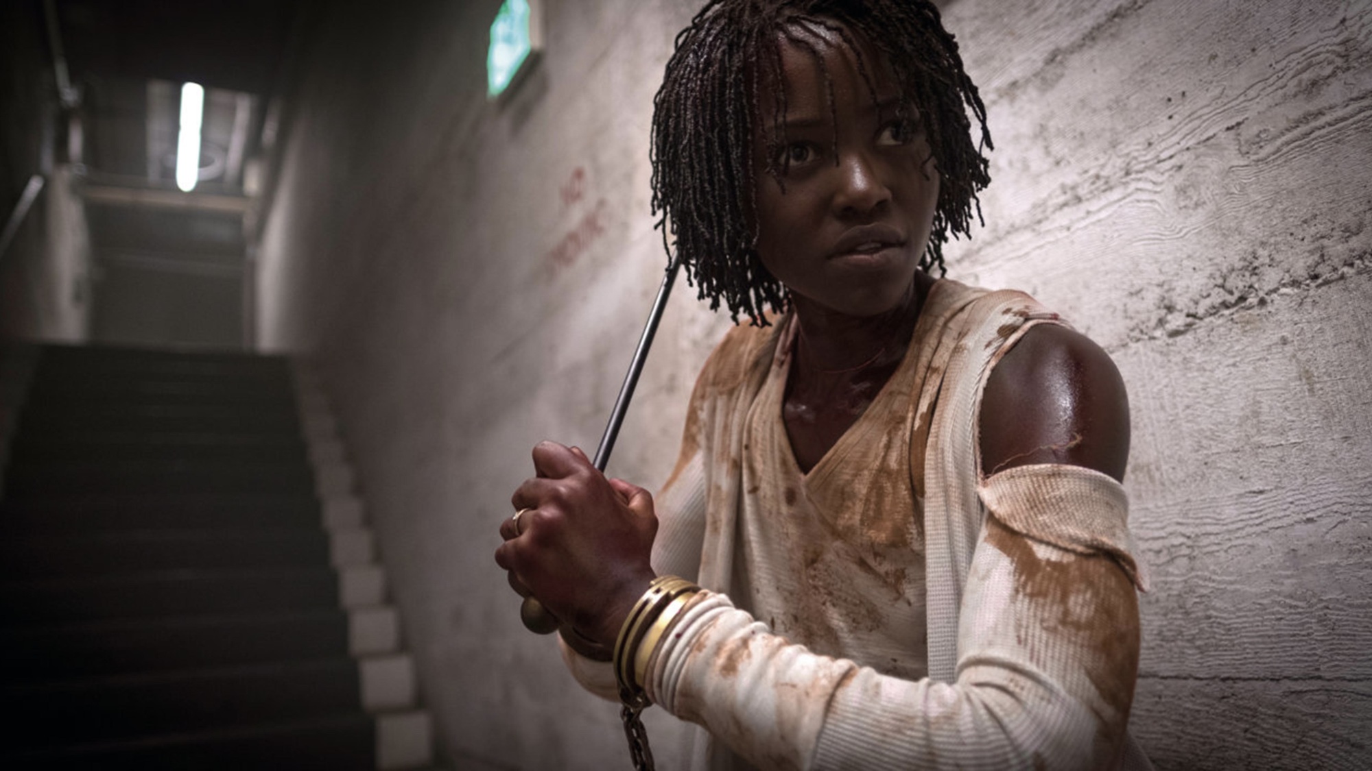 A Black woman with a metal weapon in a dim tunnel, covered in blood.